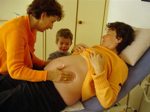 Hebamme bei Schwangerschaftskontrolle. Es werden mit den Händen die Lage des Kindes bestimmt.